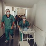 Healthcare workers in surgical attire transporting a newborn in a hospital corridor.